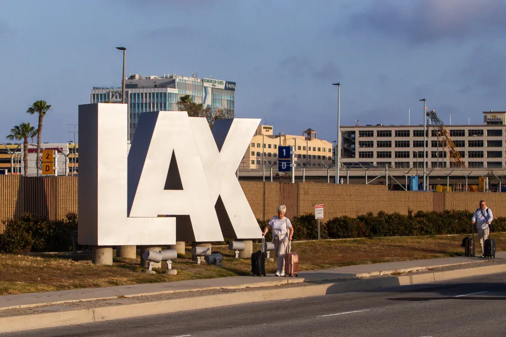 People with luggage near the LAX sign on Sepulveda Blvd.