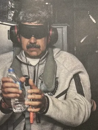 Venezuelan President Nicolas Maduro is shown blindfolded, wearing ear protection, a grey hoodie, and a life vest, holding a water bottle.