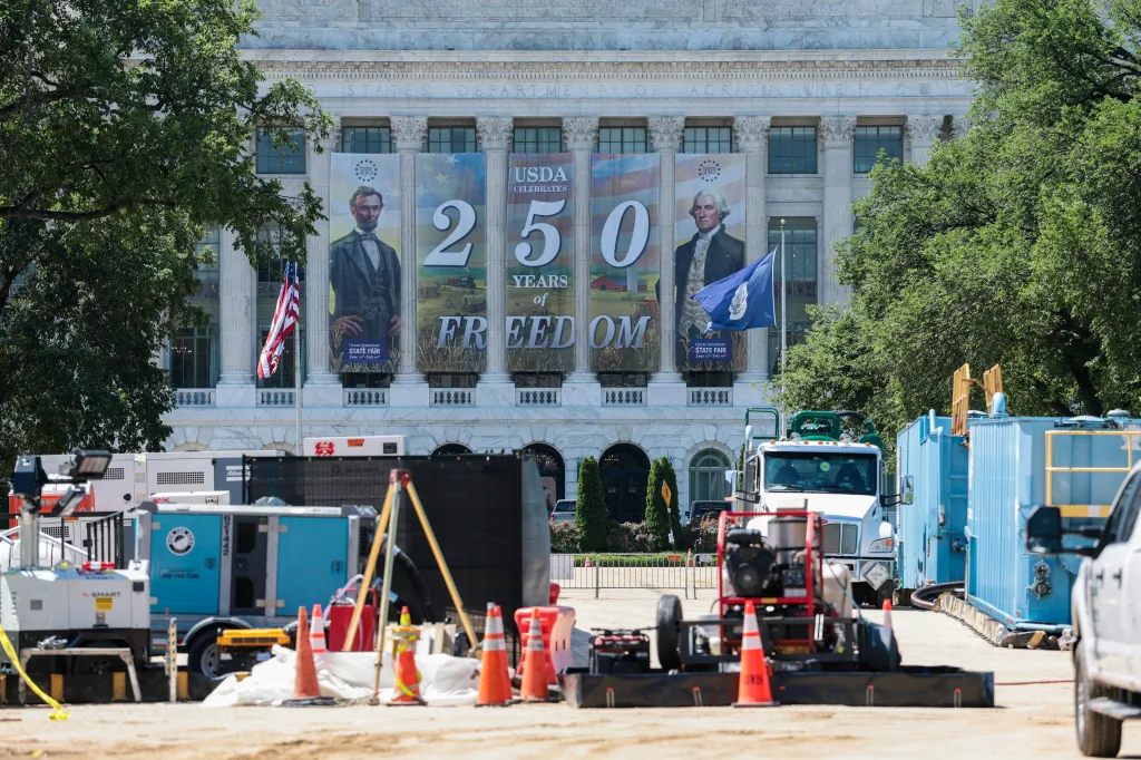 Construction equipment and barriers in front of the USDA building with banners celebrating "250 Years of Freedom."