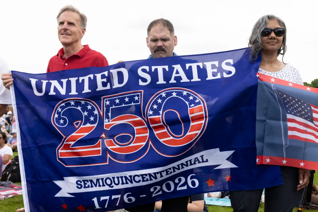 Three people holding a "United States 250 Semiquincentennial 1776-2026" flag.