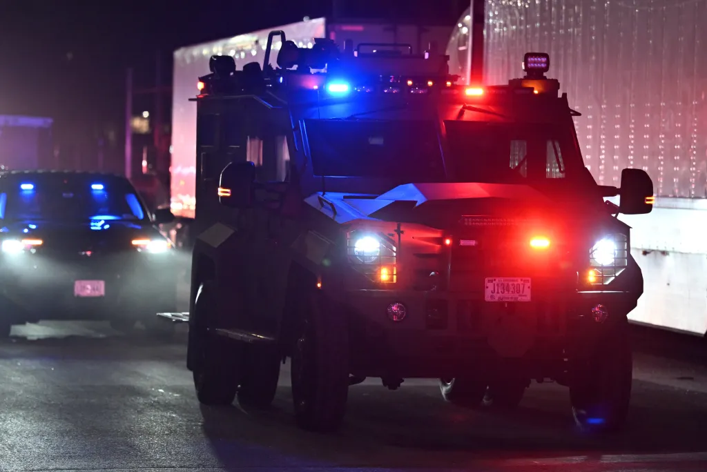 A tactical vehicle with flashing red and blue lights drives at night, part of the motorcade transporting Nicolás Maduro.