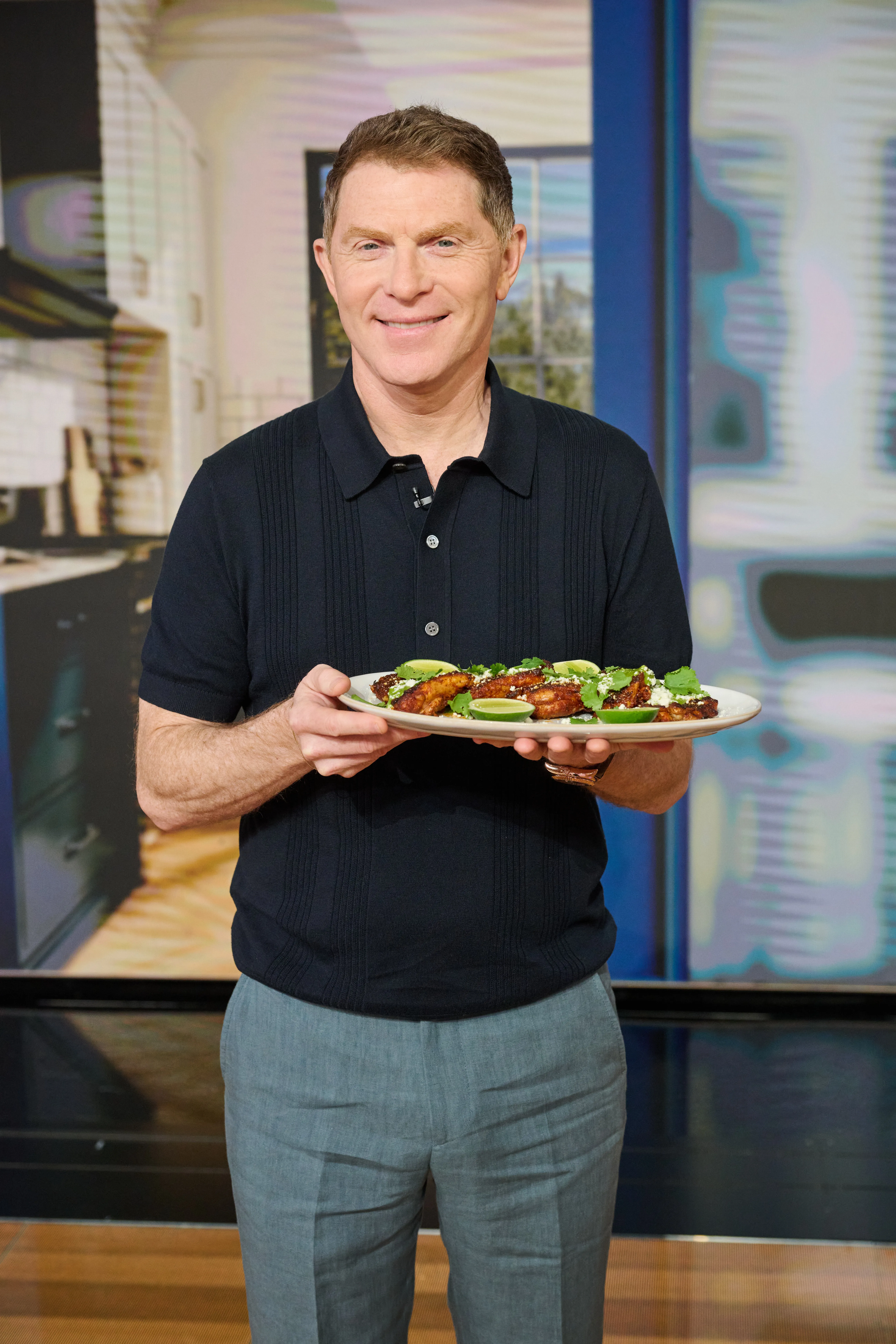 Bobby Flay holding a plate of chicken wings with cilantro and lime.