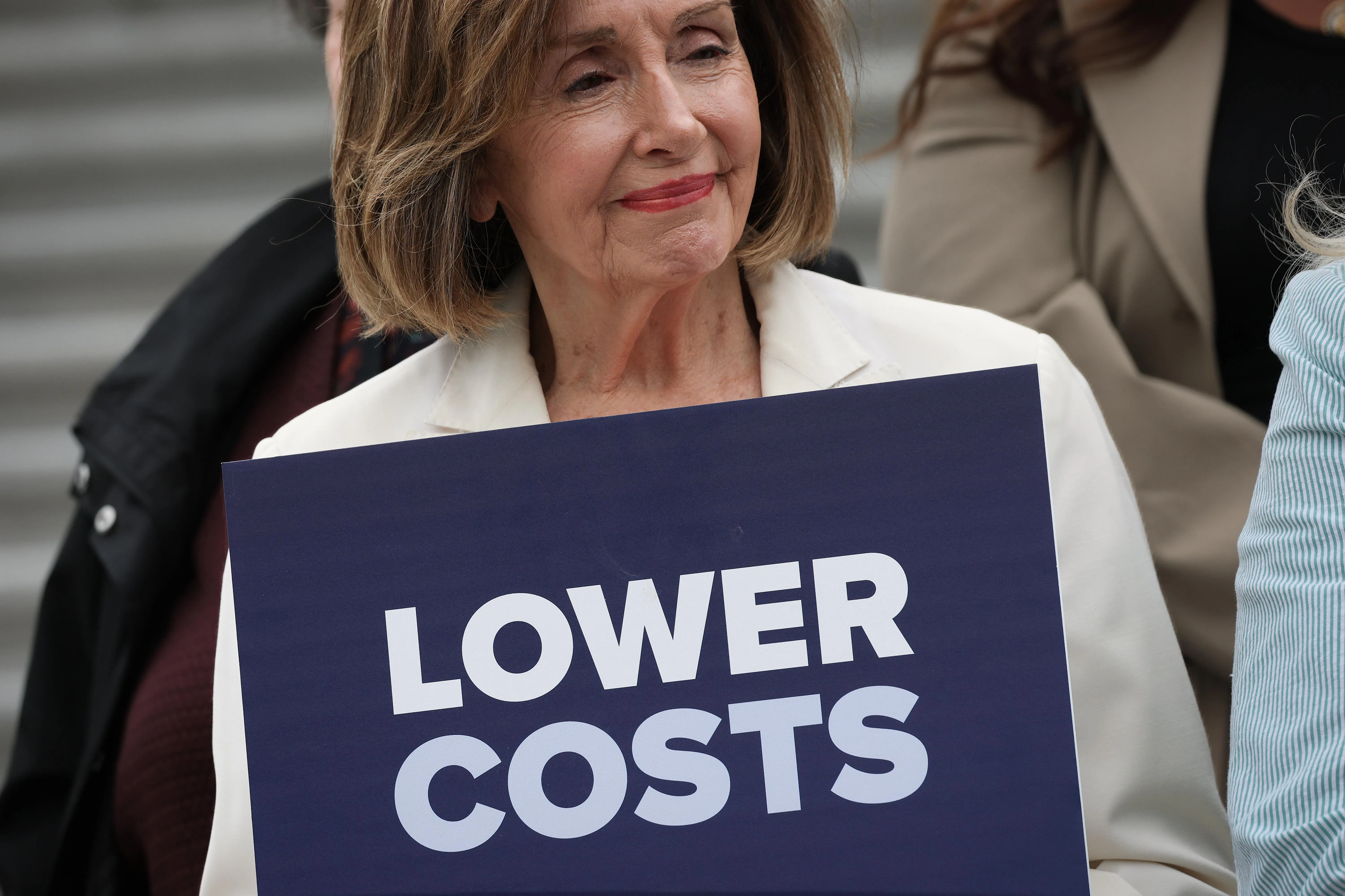Pelosi holding a sign that says “lower costs”