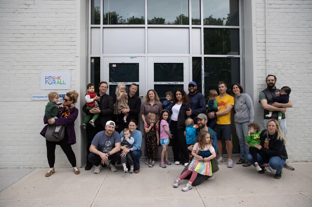 A group of parents with their young children standing in front of the "Pre-K for All" building.