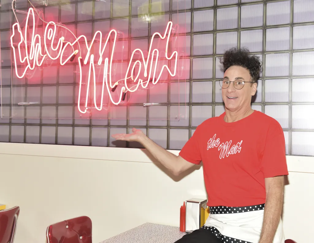 Ed Alonzo in costume as Max, with a neon "The Max" sign behind him.