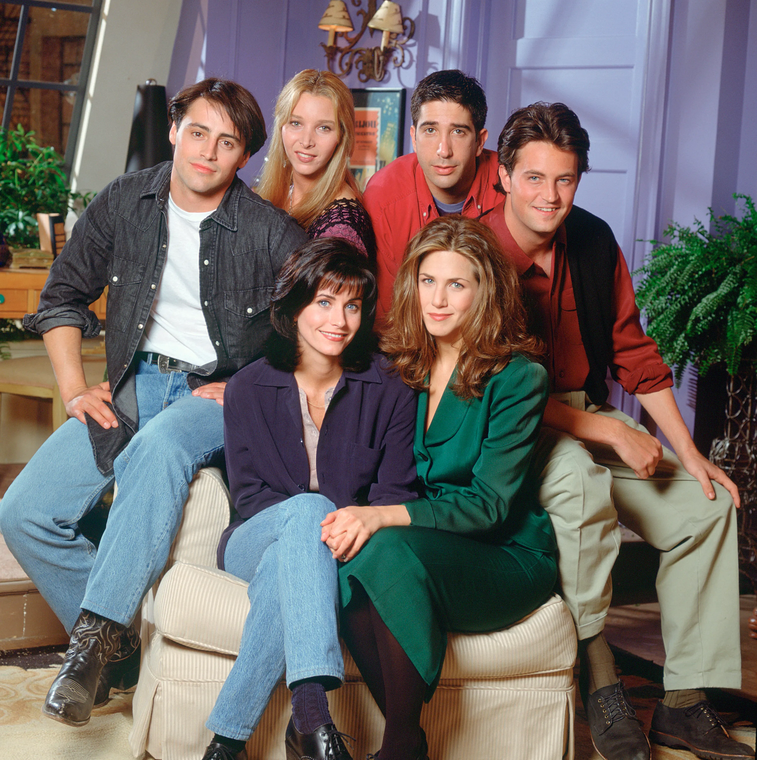 Group portrait of the cast of Friends in character, with the women seated in front of the men.