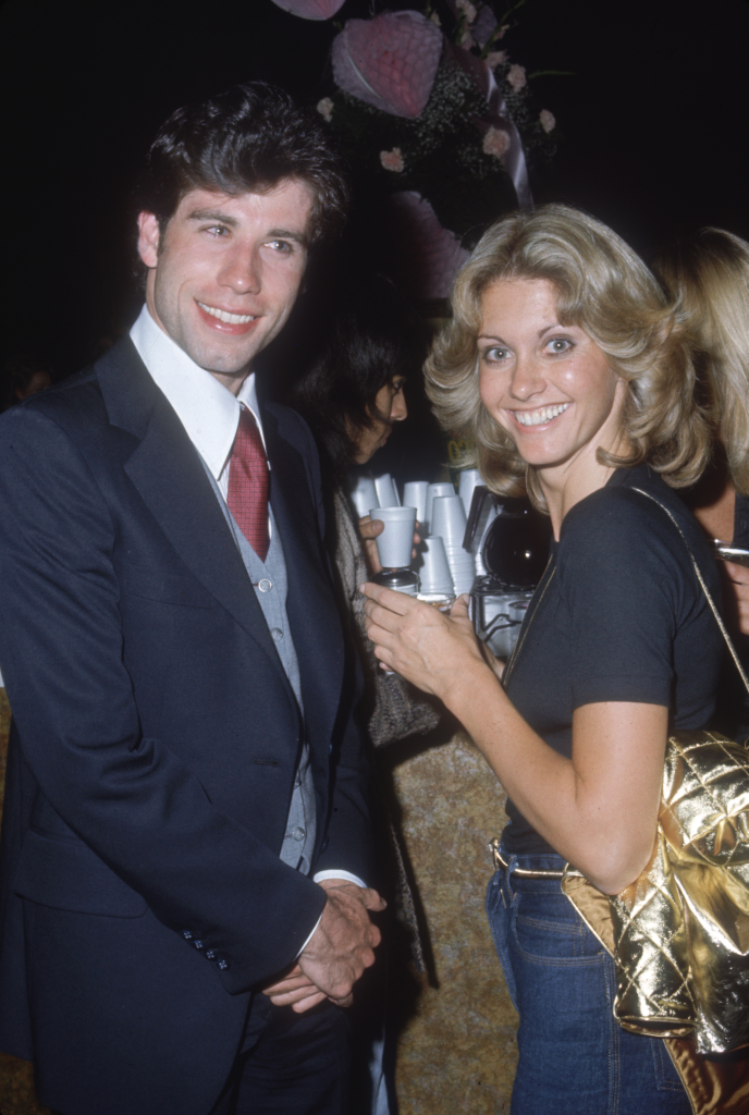 John Travolta in a suit and Olivia Newton-John in a black shirt and jeans at a Grease party.