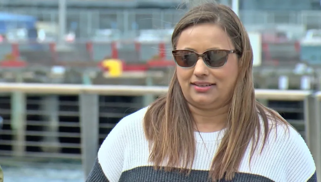 Dharmi Mehta, wearing sunglasses and a striped sweater, looking forward.