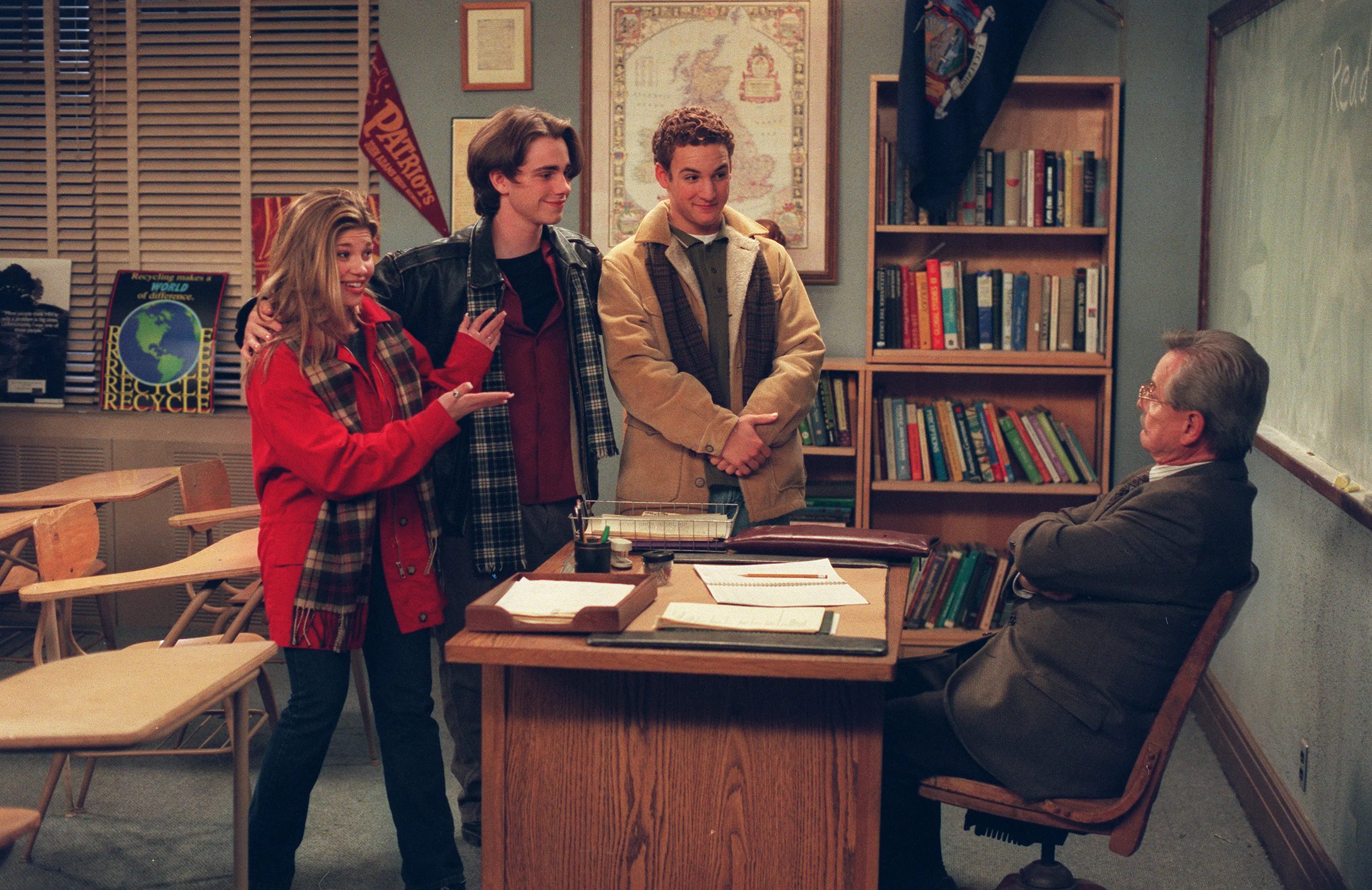 Danielle Fishel, Rider Strong, and Ben Savage standing at a teacher's desk talking to William Daniels.