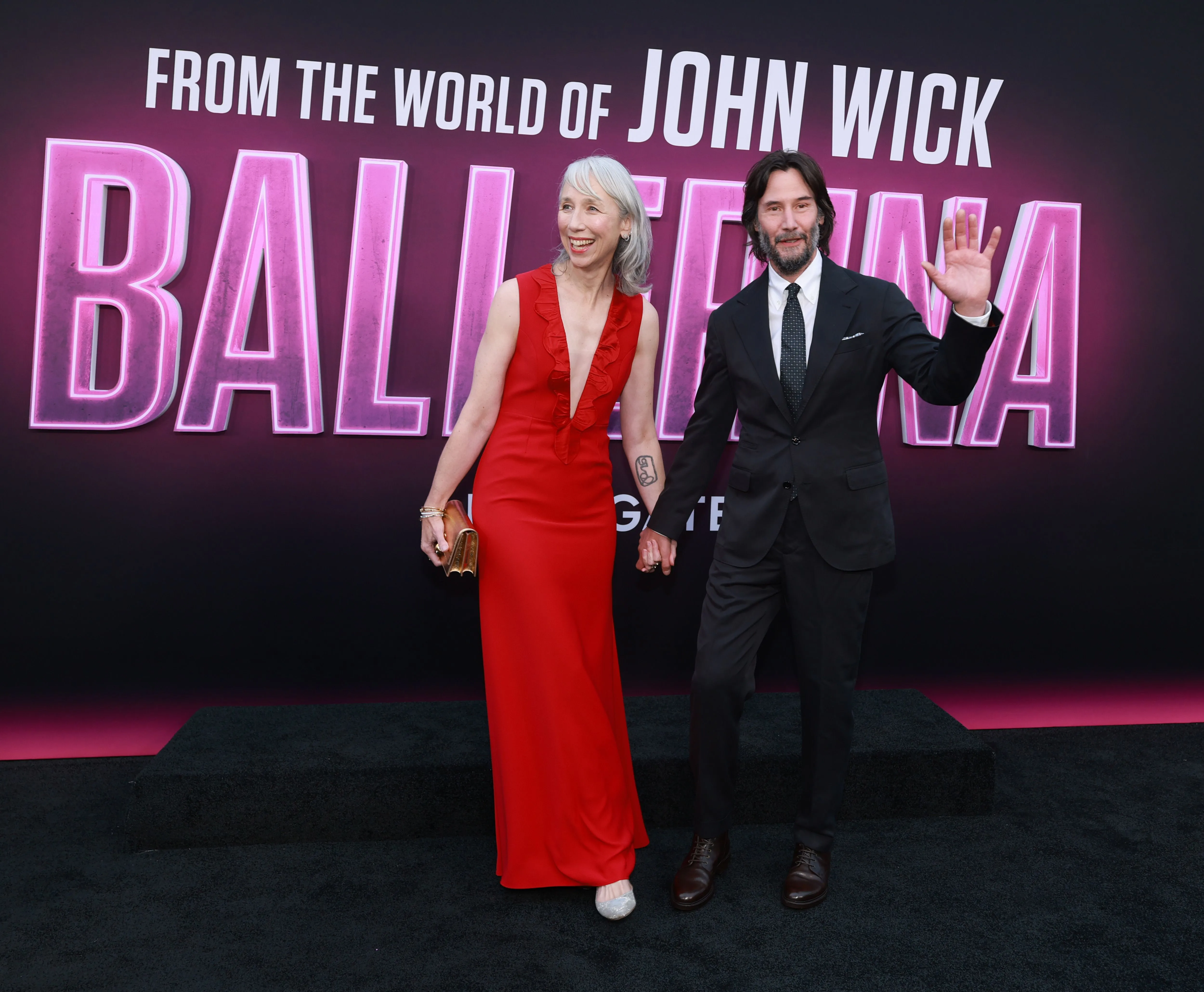 Alexandra Grant in a red dress and Keanu Reeves in a black suit holding hands at the "Ballerina" premiere.