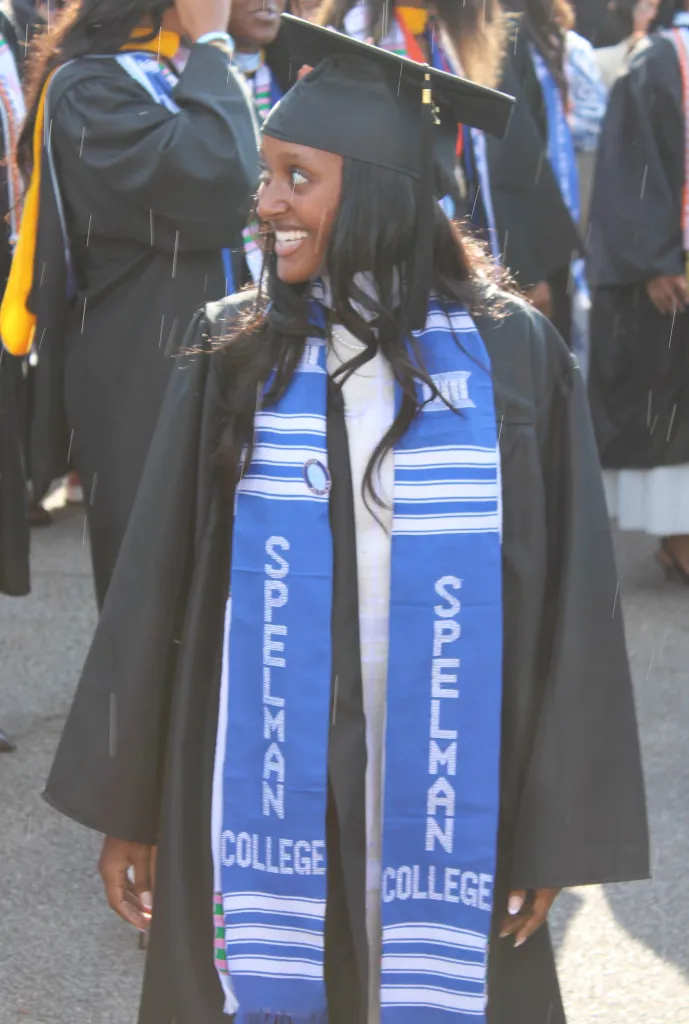 Zahara Jolie-Pitt smiling in her graduation cap and gown with a blue "Spelman College" sash.