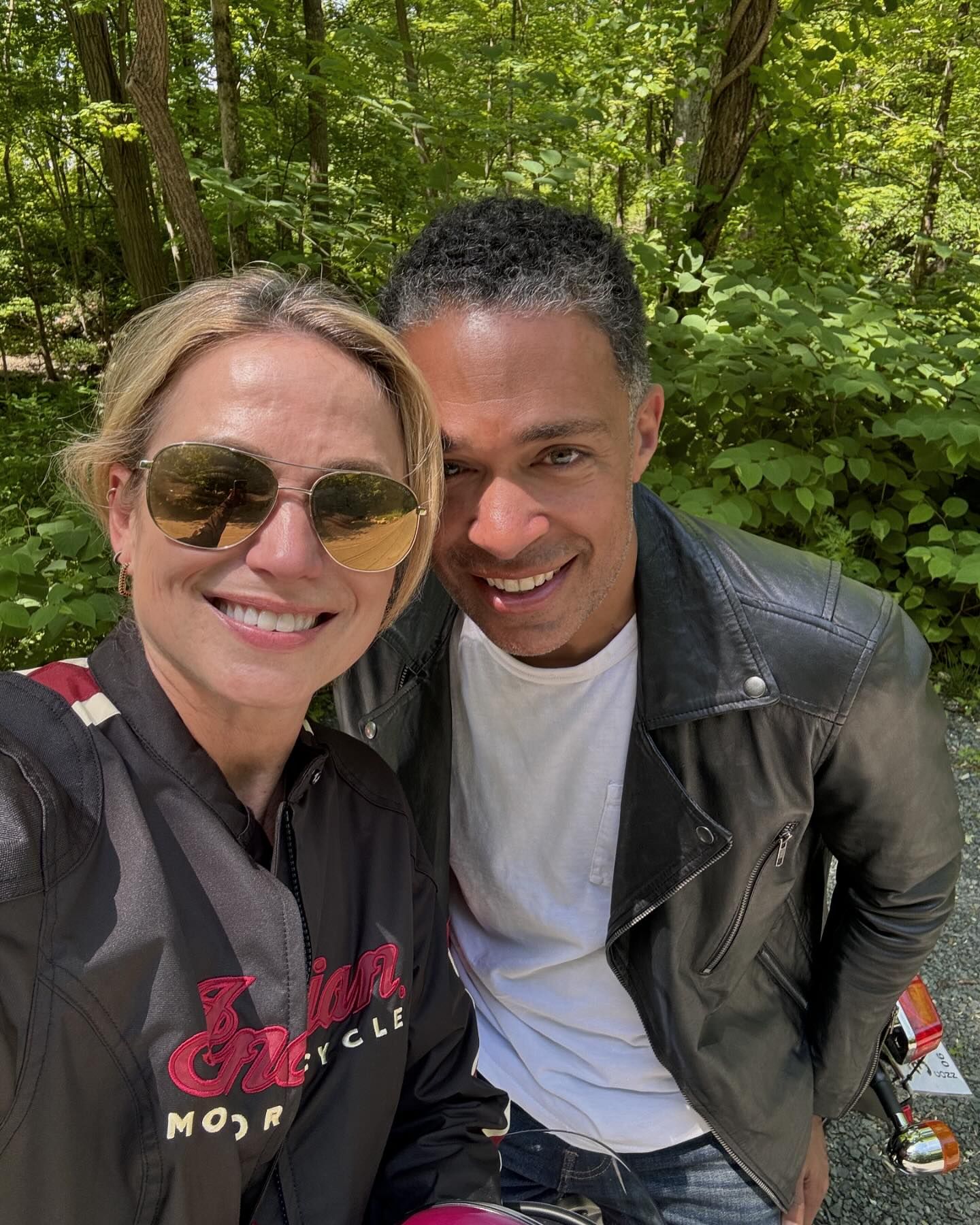 Amy Robach and TJ Holmes posing for a selfie in front of a wooded area.