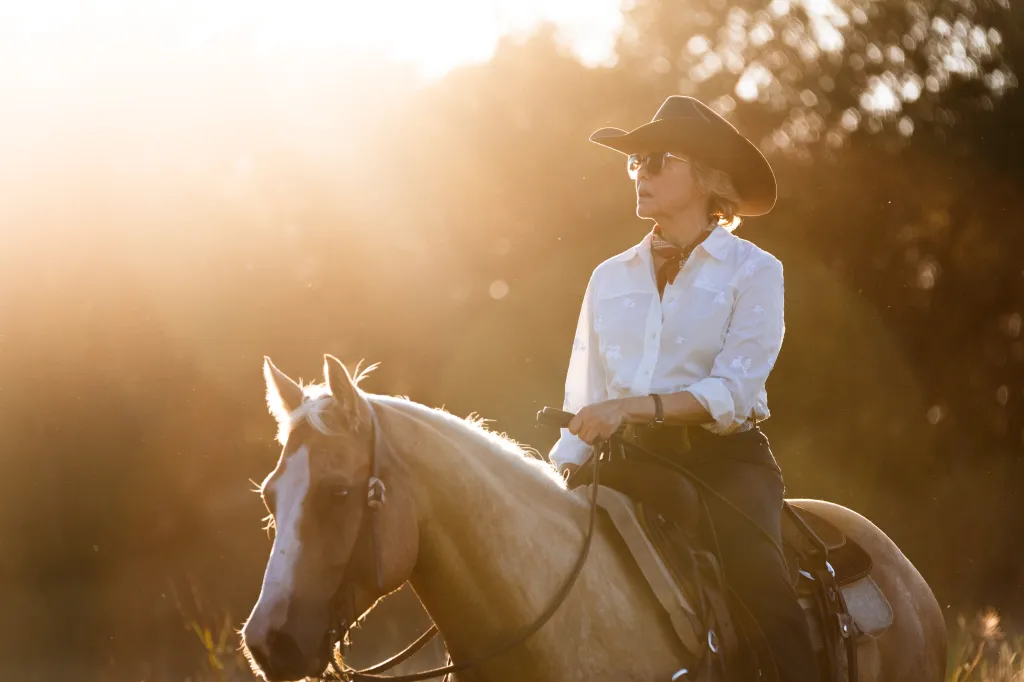 Annette Bening as Beulah Jackson in a cowboy hat and sunglasses, riding a horse.