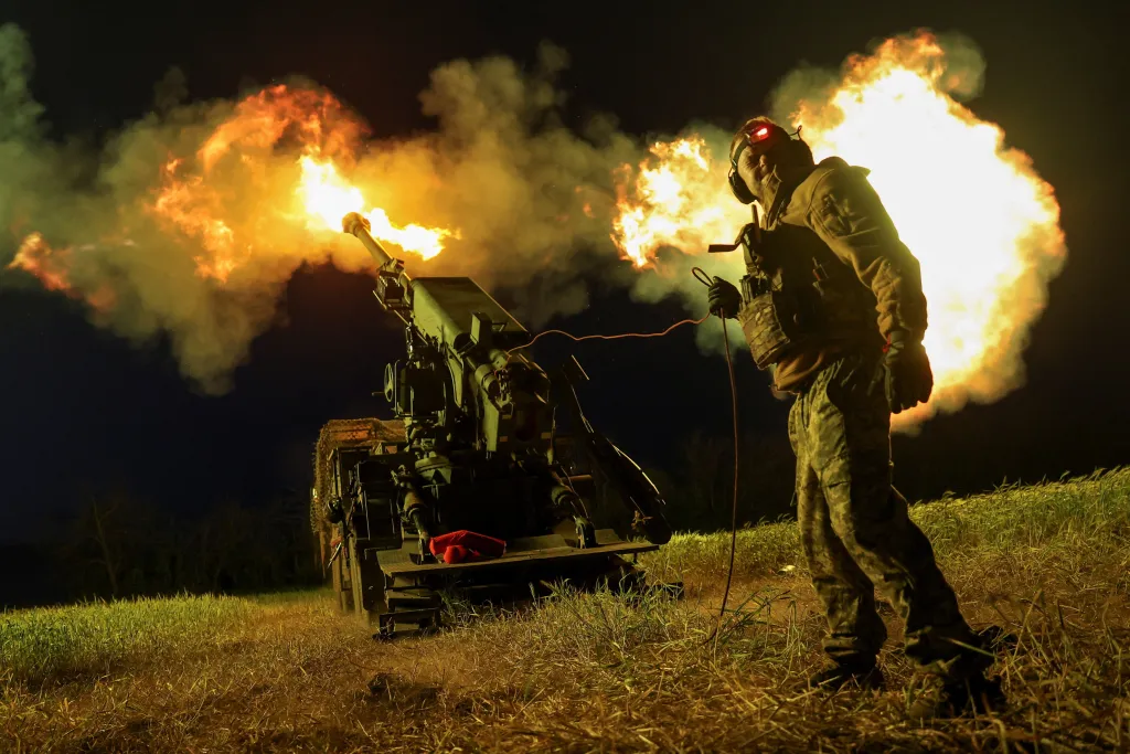 Ukrainian serviceman firing a self-propelled howitzer at night, causing a large muzzle flash.