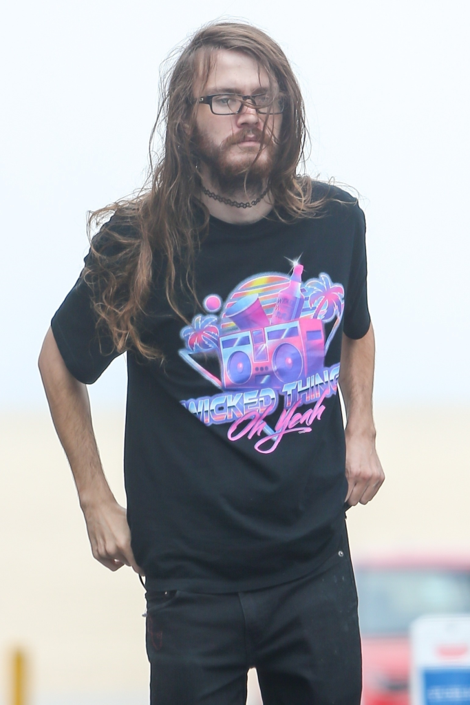 Chance Hogan wearing a black t-shirt with a colorful graphic design, black pants, and glasses, standing on Venice Beach.
