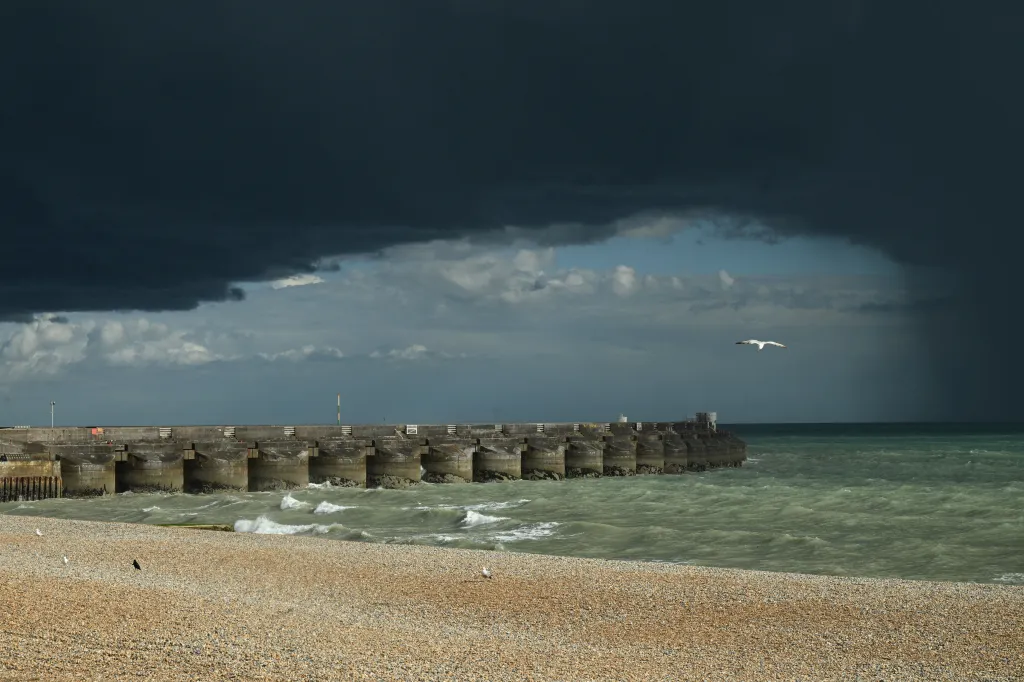 A bird flying near a concrete sea defense structure under dark clouds in Brighton.