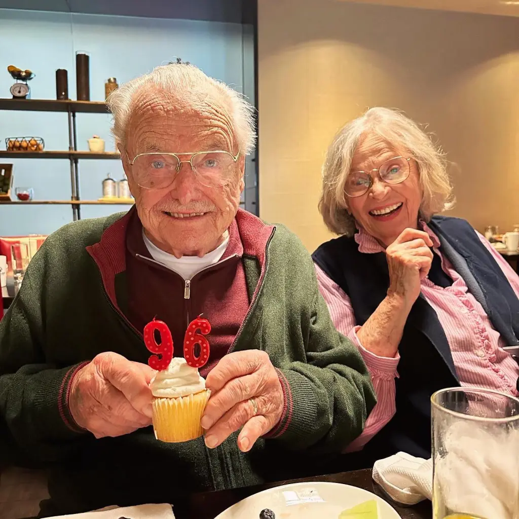 William Daniels holding a cupcake with a "96" candle, next to Bonnie Bartlett.