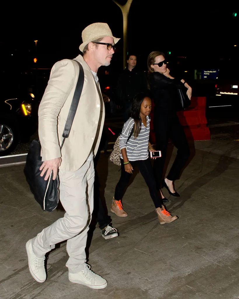 Brad Pitt, Angelina Jolie, and their children, Maddox and Zahara Jolie-Pitt, walk at LAX at night.
