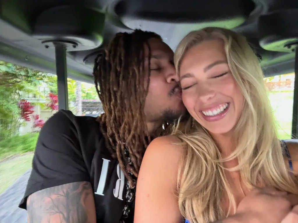 Brandon Clarke kisses his fiancée Amber Lorraine on the cheek, who is smiling with closed eyes, as they sit in a golf cart.