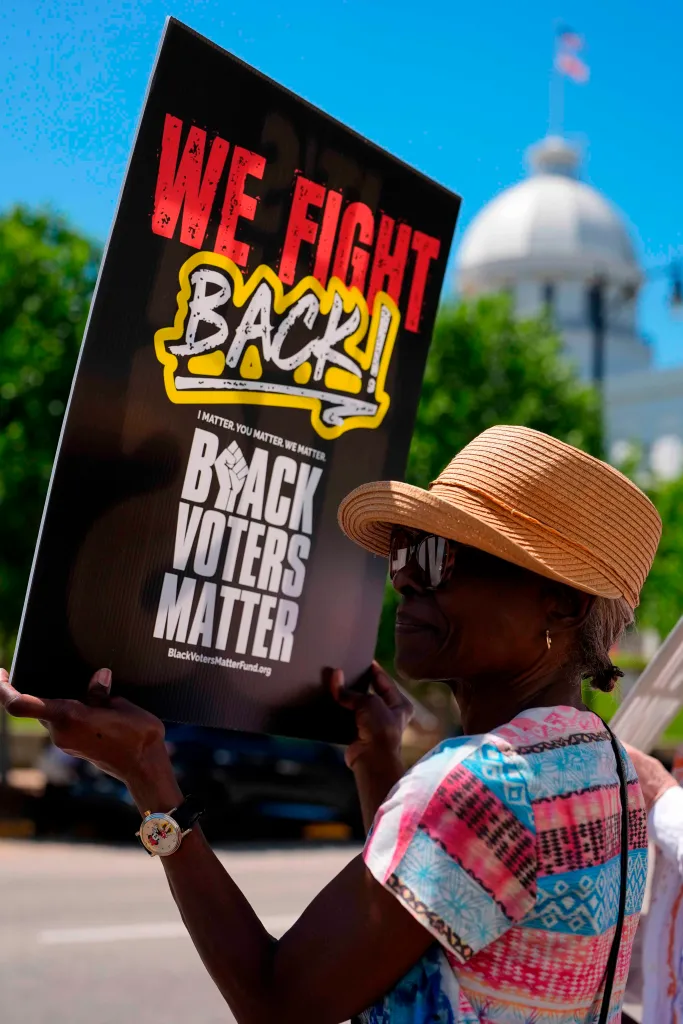 A woman protesting with a sign that reads "WE FIGHT BACK! BLACK VOTERS MATTER" in front of the Alabama State Capitol.