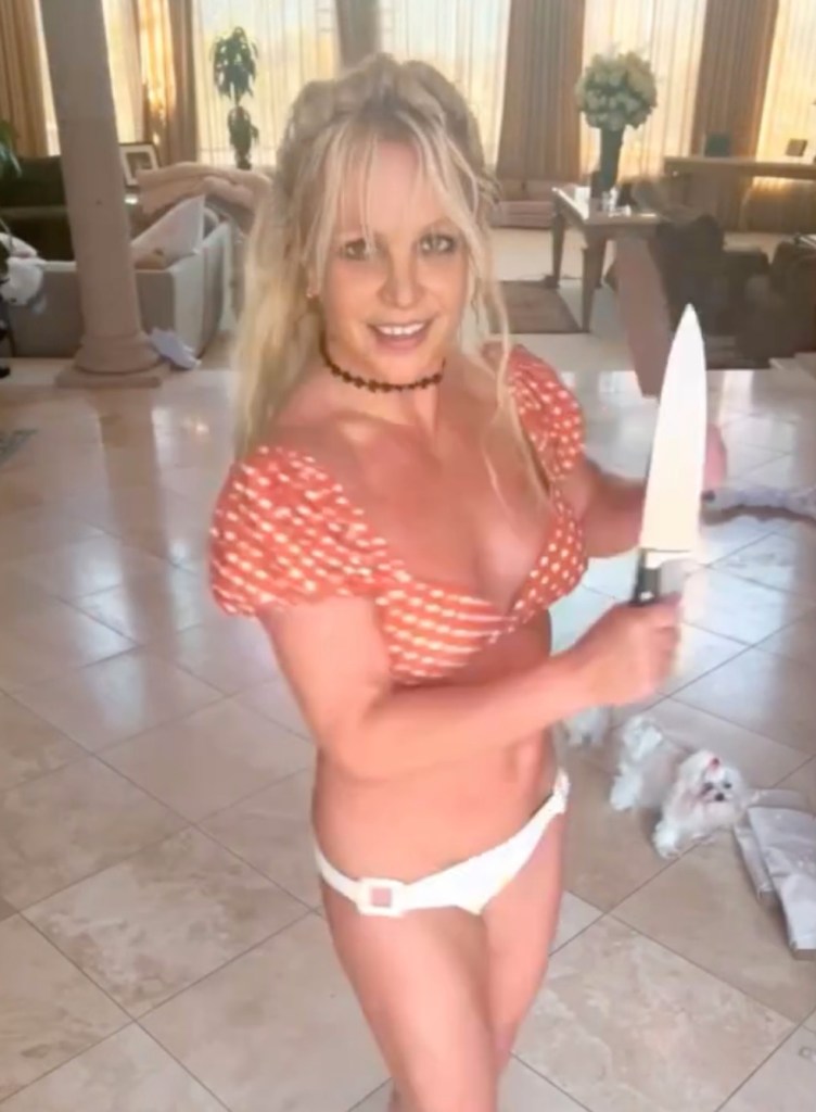 Britney Spears in an orange and white polka-dot top and white bikini bottoms, holding a large knife.