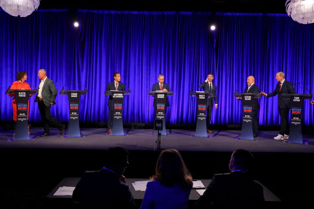 Candidates Katie Porter, Chad Bianco, Antonio Villaraigosa, Xavier Becerra, Matt Mahan, Steve Hilton, and Tom Steyer stand at podiums during a California gubernatorial debate.