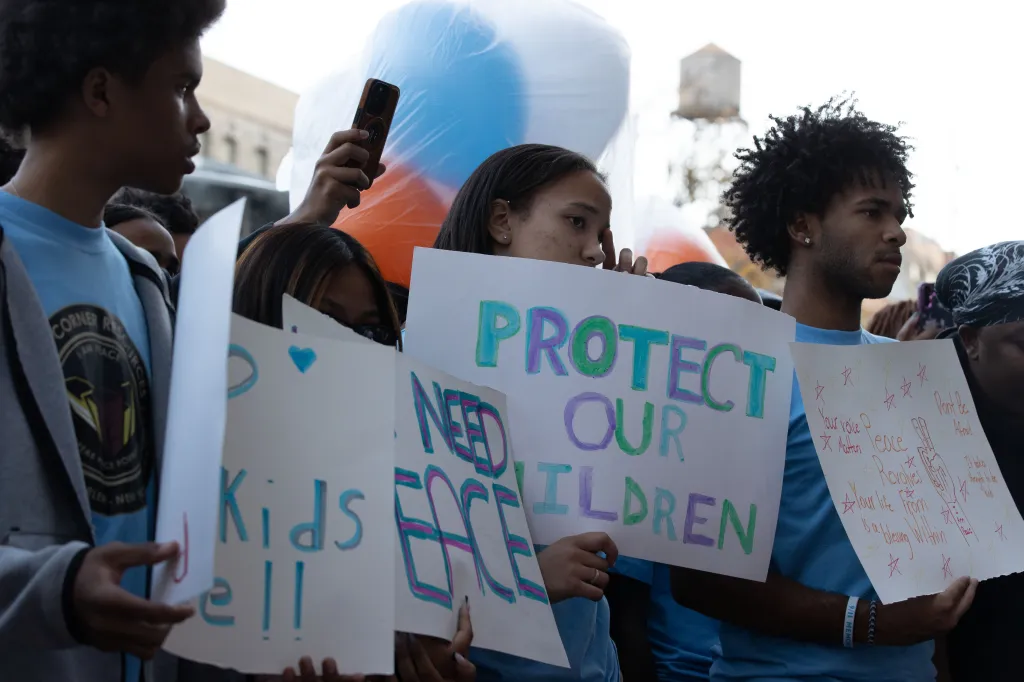Young activists hold posters reading "Protect Our Children" and "Your voice matters. Peace revolves. Your life is a blessing within" at a balloon release in memory of Jahmeik Modlin.