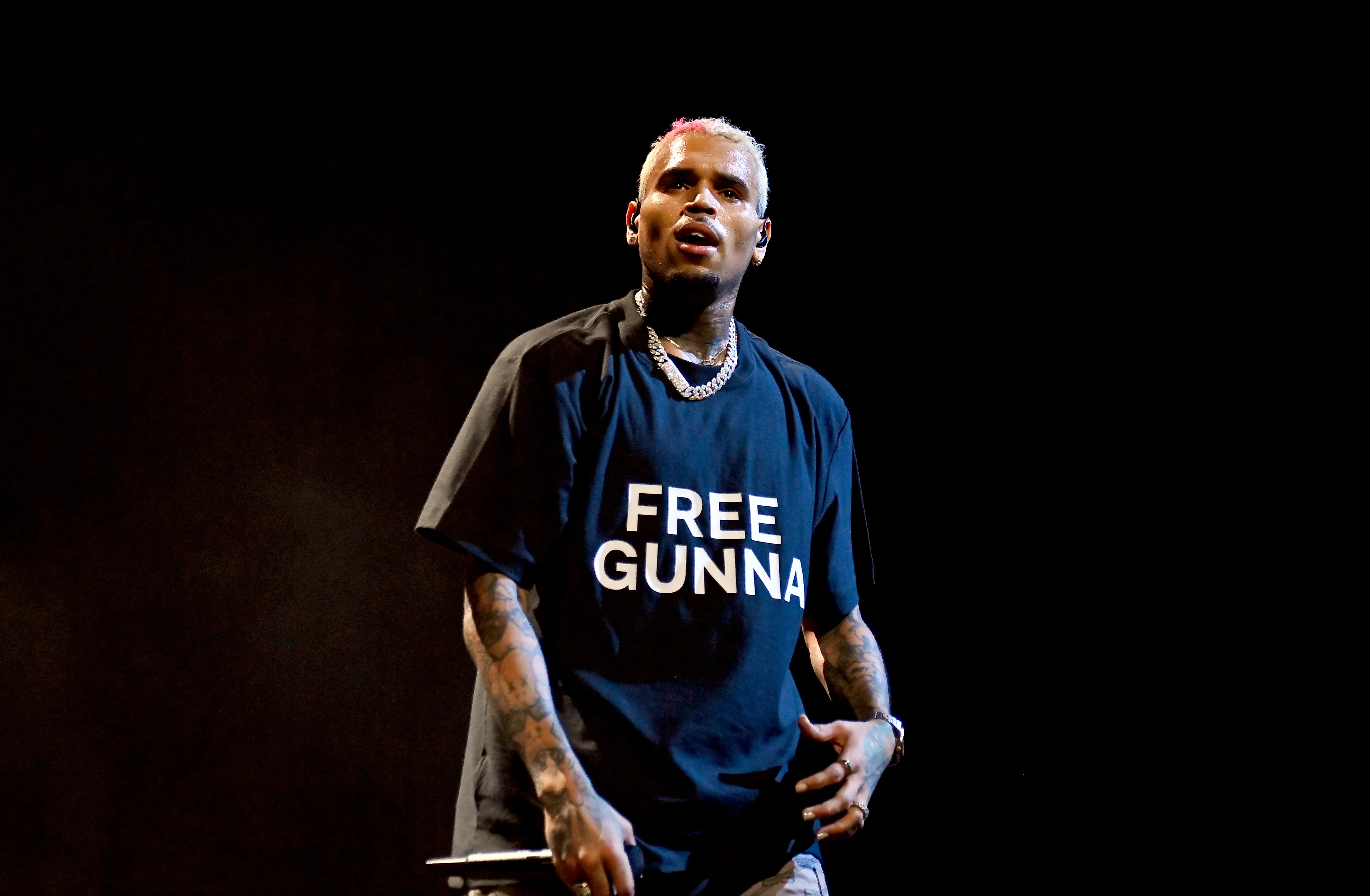 Chris Brown performing onstage in a black t-shirt that says "FREE GUNNA" in white letters.