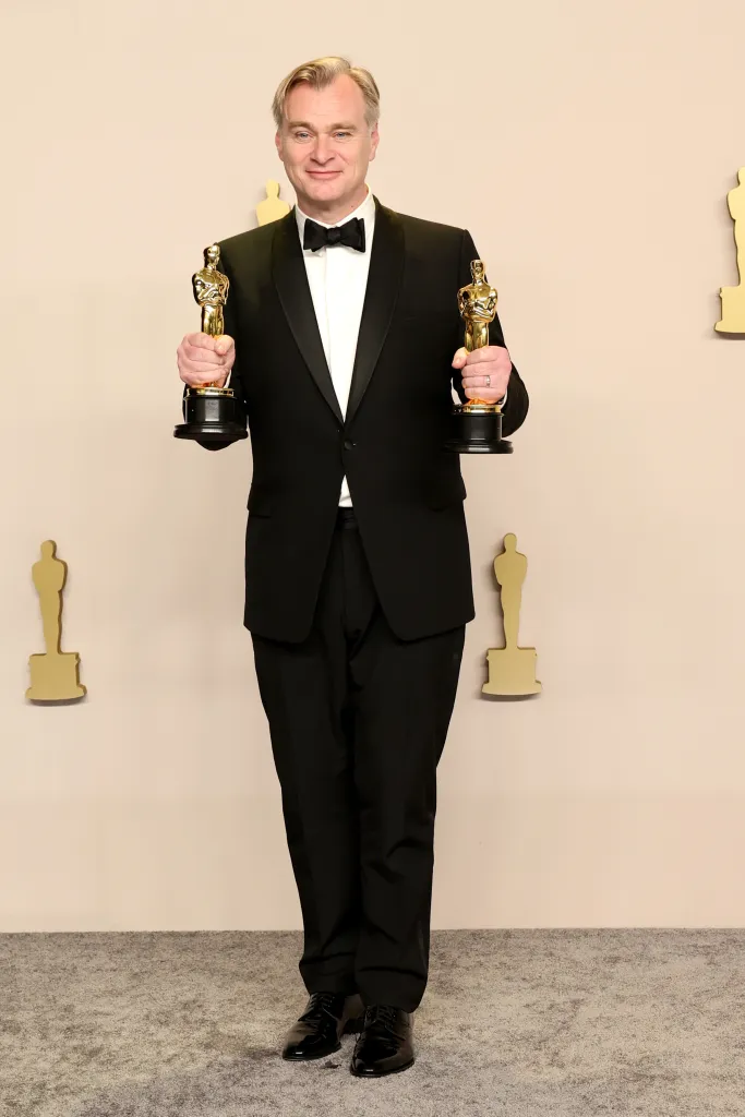 Christopher Nolan holding two Academy Awards for Best Directing and Best Picture.