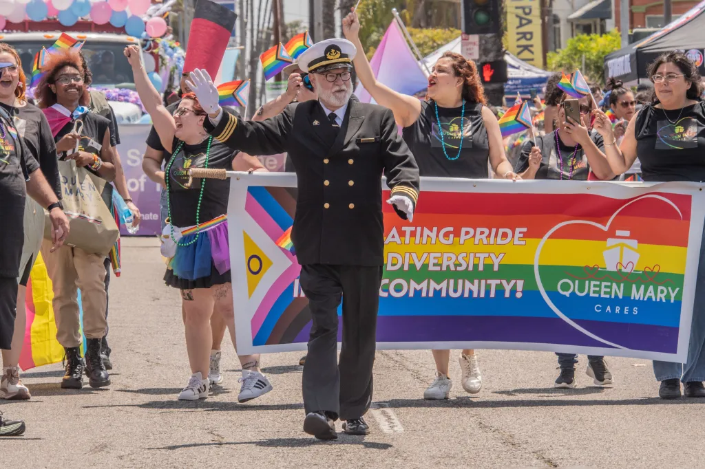 People in a Long Beach Pride Parade holding a banner that reads "Celebrating Pride Diversity Community!" and "Queen Mary Cares"