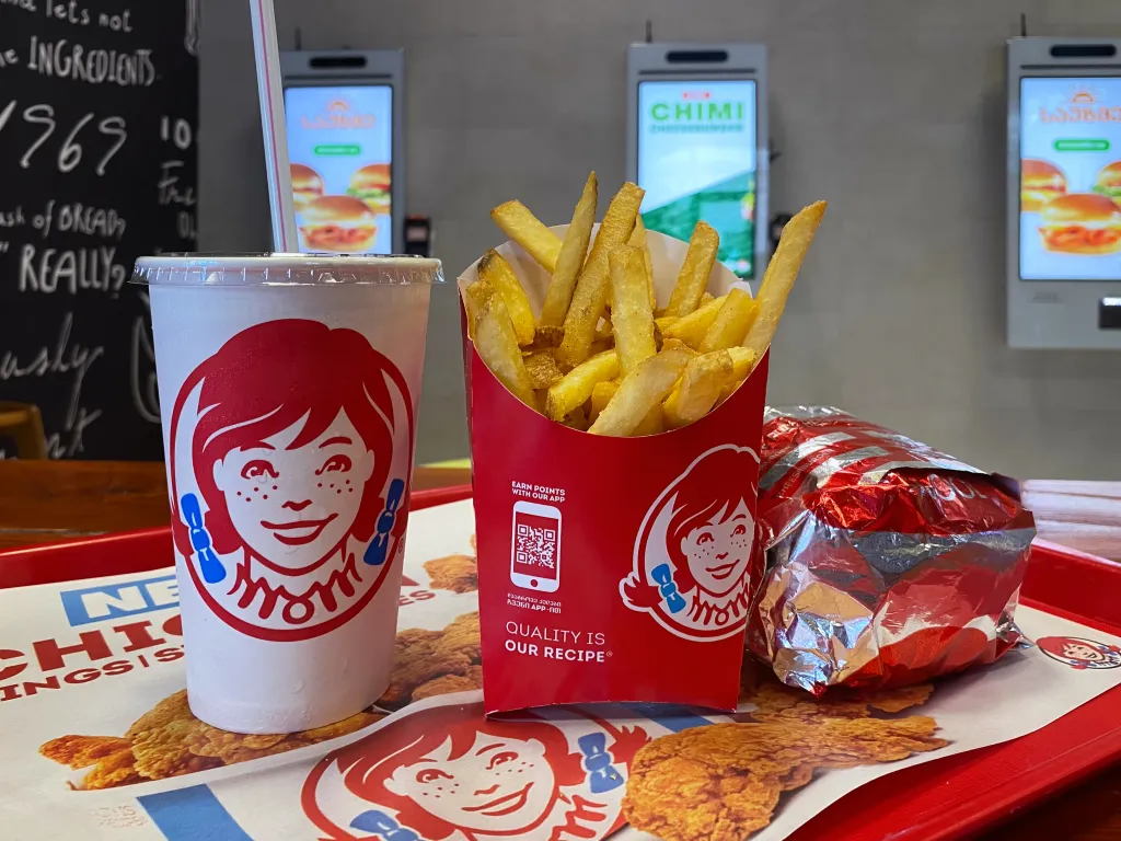 A Wendy's combo meal, consisting of a drink, fries, and a wrapped burger, on a red tray.