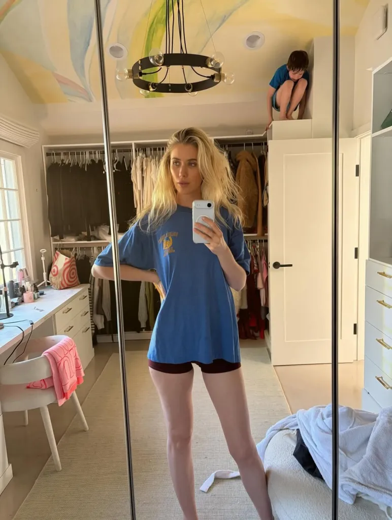 Comedian Laura Clery takes a mirror selfie while her child peeks over a wall.