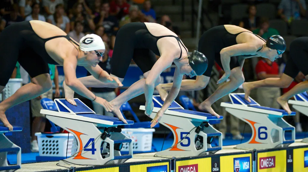 Swimmers Megan Romano, Missy Franklin, and Allison Schmitt diving at the start of a 100-meter freestyle preliminary heat.