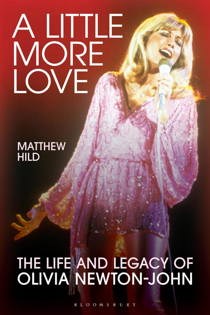 Cover of the biography "A Little More Love: The Life and Legacy of Olivia Newton-John" by Matthew Hild, featuring a photo of Olivia Newton-John singing into a microphone.