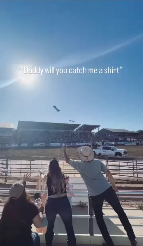 A t-shirt tossed into a crowd at a rodeo event, with text overlay "Daddy will you catch me a shirt".