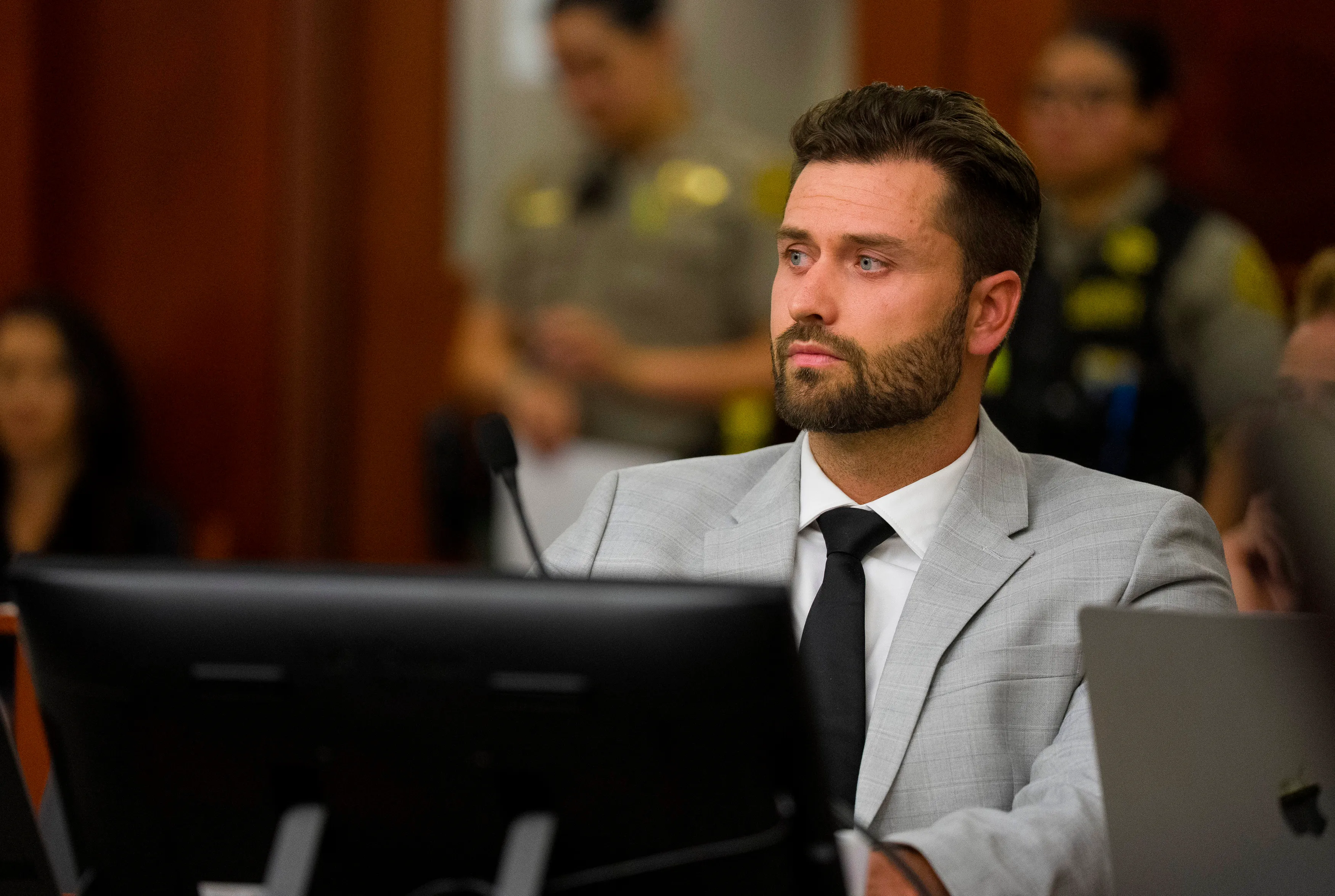 Dakota Mortensen in court, wearing a gray suit and black tie, appearing serious during proceedings.