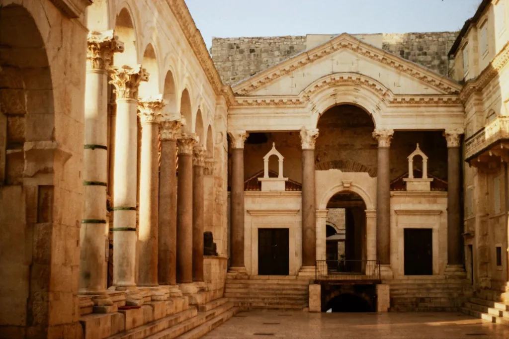 The Peristyle, a central court in Diocletian's Palace, with a row of columns and arches on the left, and a monumental archway with smaller niches and a doorway on the right.