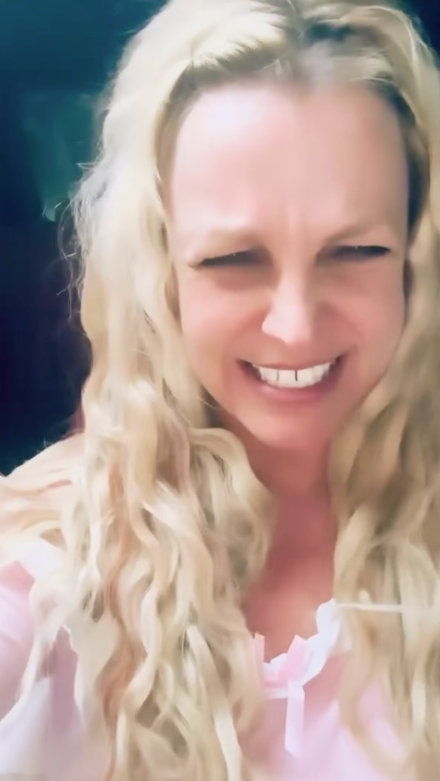 Britney Spears with a wide smile, squinting her eyes, and wearing a pink top with white ruffles.