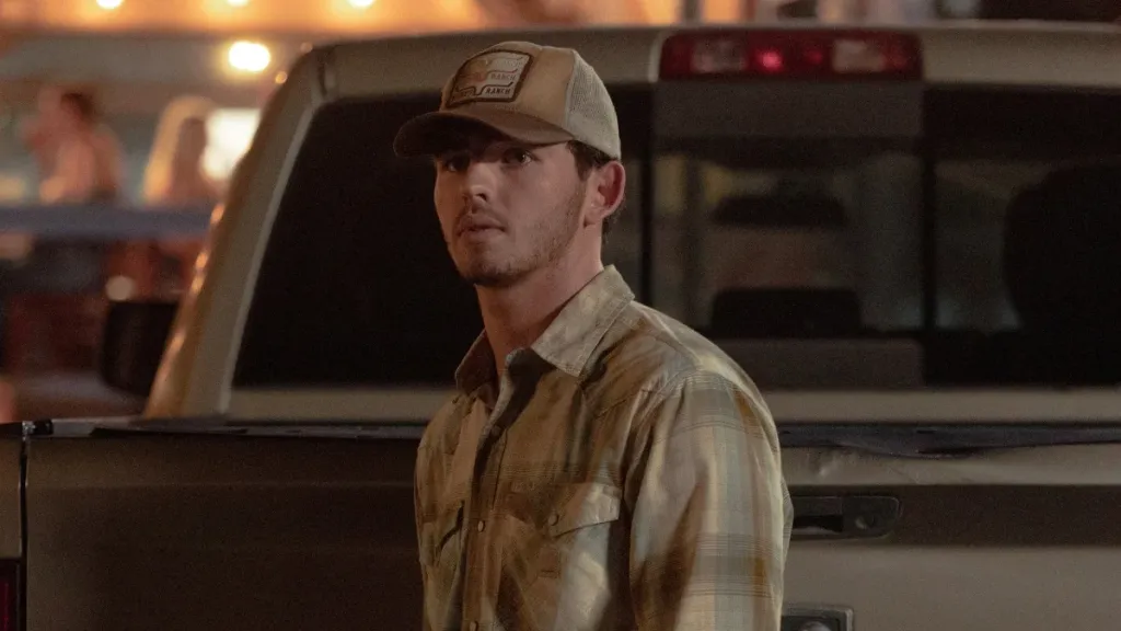  young man in a tan plaid flannel shirt and a trucker cap reading 