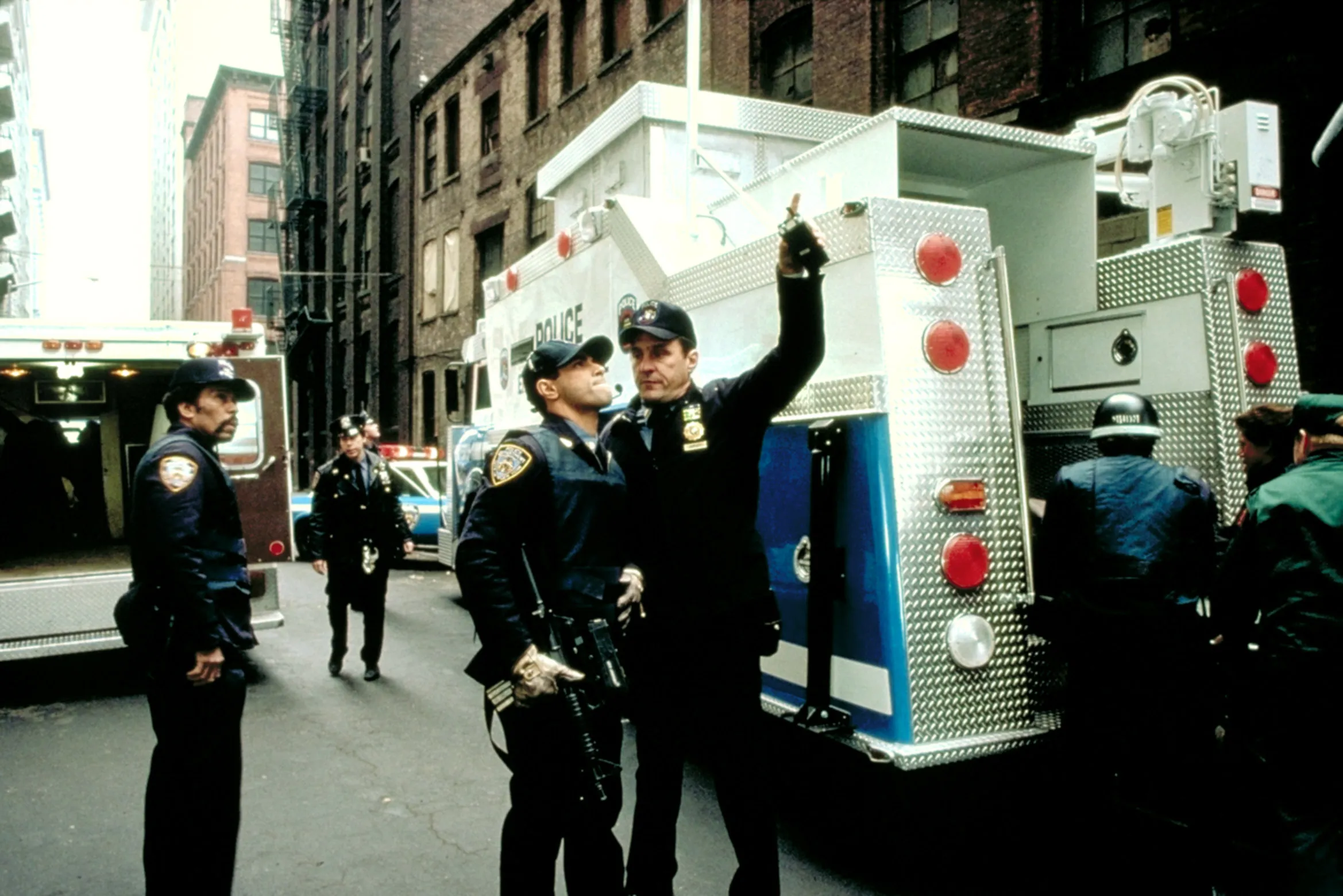 Beau Starr and Eddie Velez looking up while standing near a police truck in a scene from "True Blue."