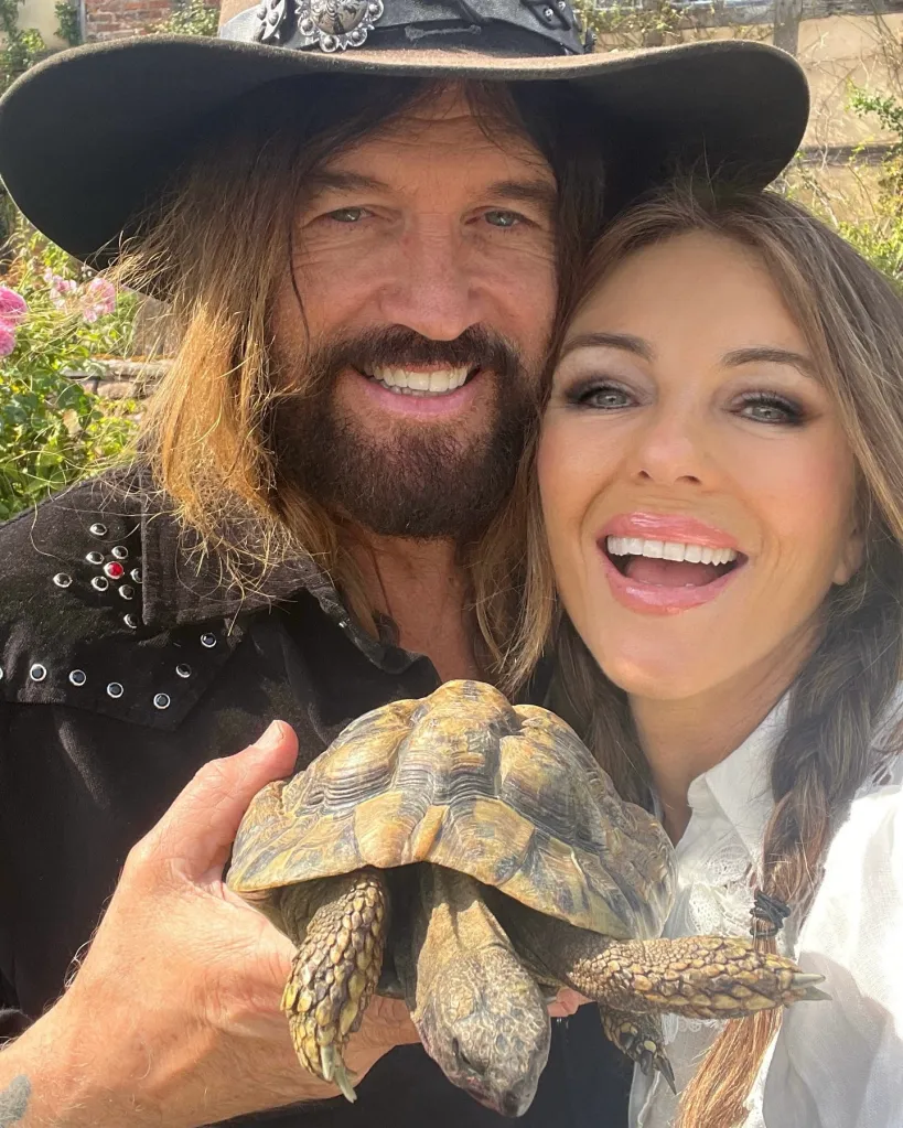 Billy Ray Cyrus and Elizabeth Hurley smile while holding a tortoise.