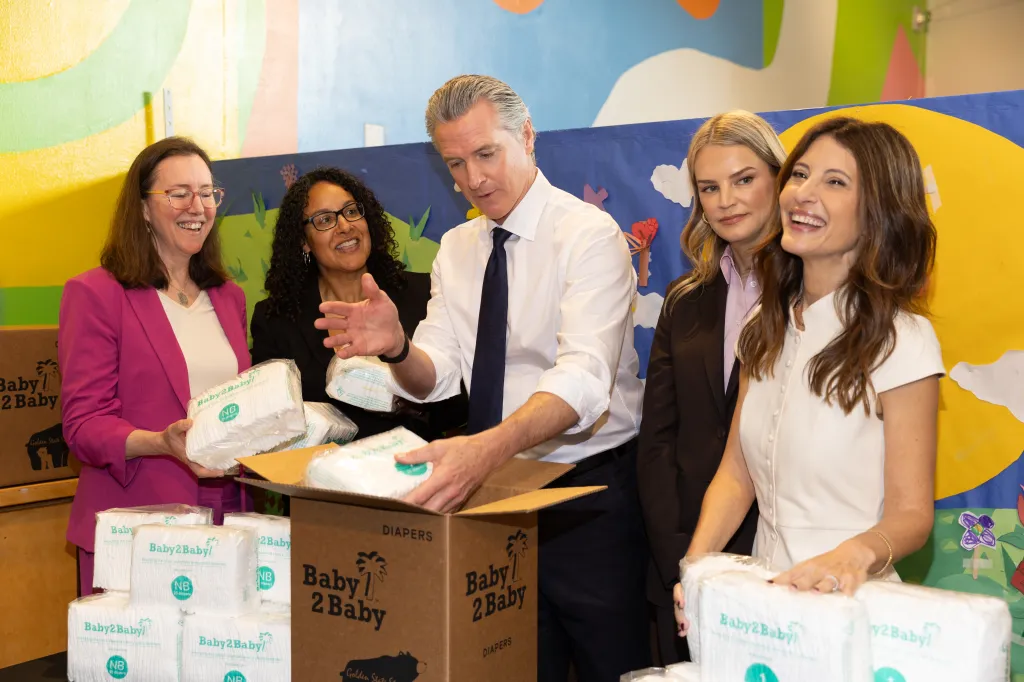 Five people, including Gavin Newsom, filling boxes with diapers at the Baby2Baby x Golden State Start event.