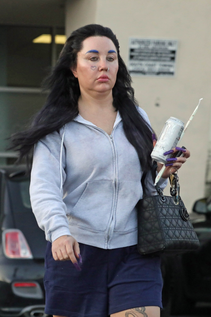 Amanda Bynes with dark hair, blue eyebrows, and a heart outline tattoo on her cheek.