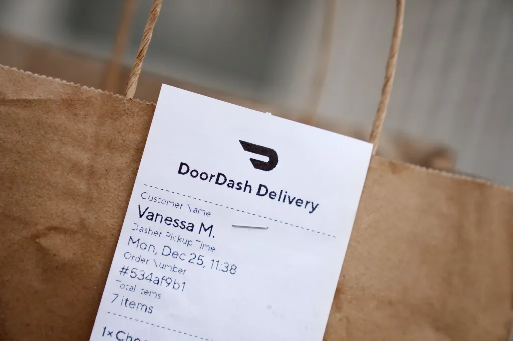 A DoorDash delivery bag with a label showing "DoorDash Delivery," customer name "Vanessa M.," and an order number.