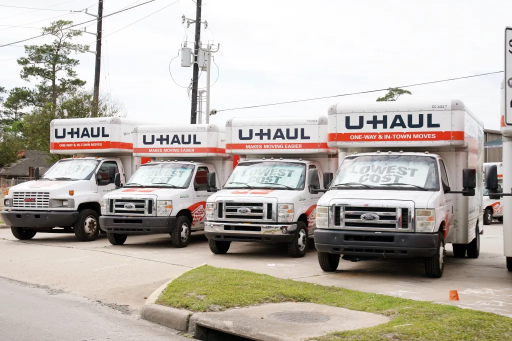 A line of white U-Haul trucks with "LOWEST COST" signs on their windshields.