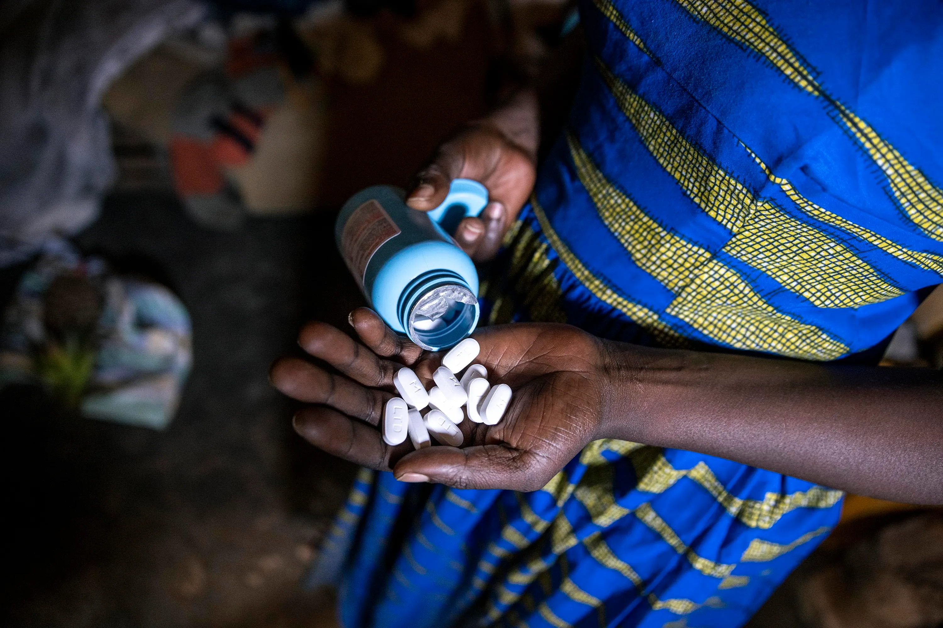 A woman holding HIV drugs in her hand wearing a blue and yellow dress.