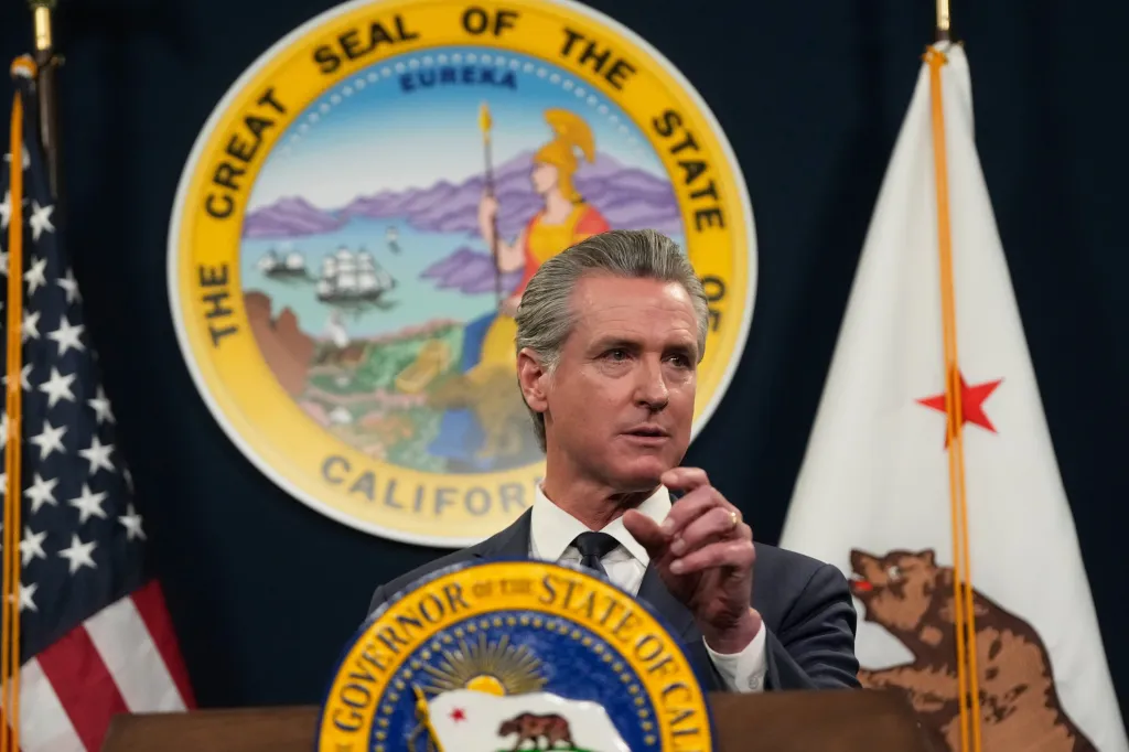 Gavin Newsom speaking at a podium with the Great Seal of the State of California behind him.