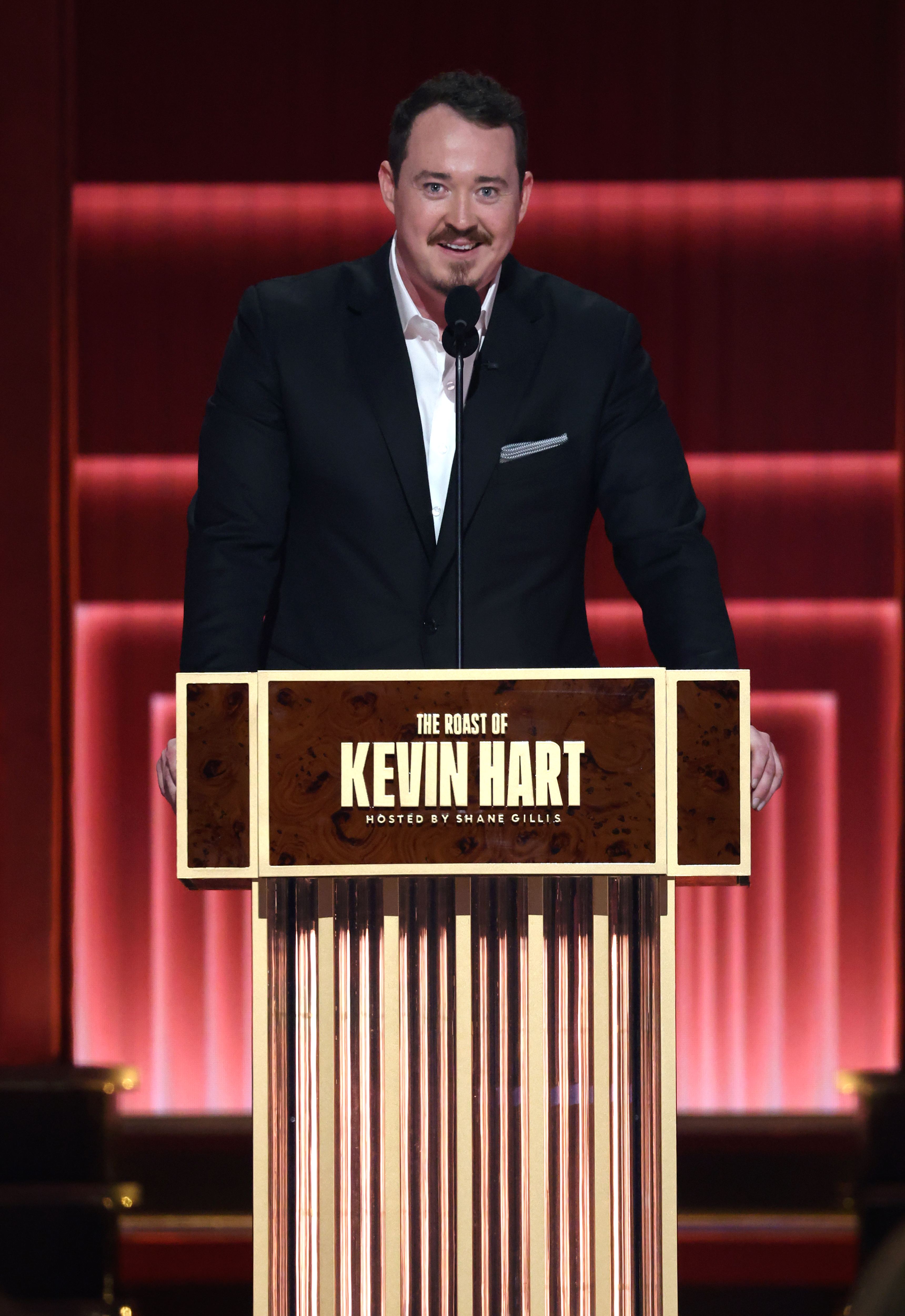 Shane Gillis speaking onstage at "The Roast of Kevin Hart" event.