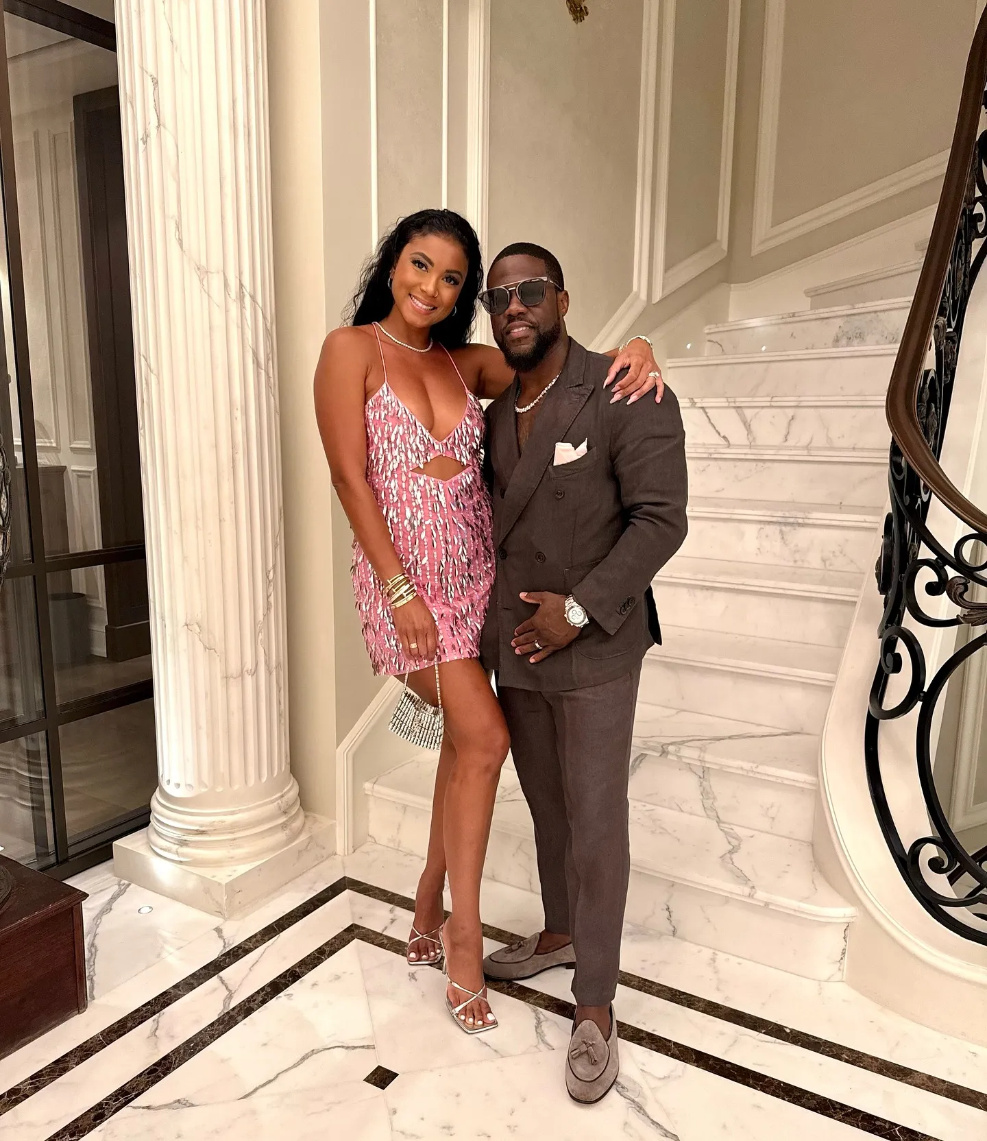 Kevin and Eniko Hart posing for a photo at the bottom of a marble staircase.