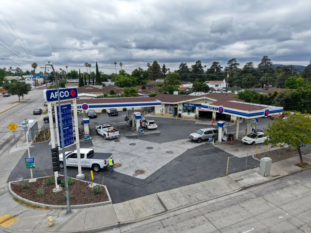 Aerial view of an ARCO gas station in Altadena, California, with vehicles at pumps and fuel prices displayed.